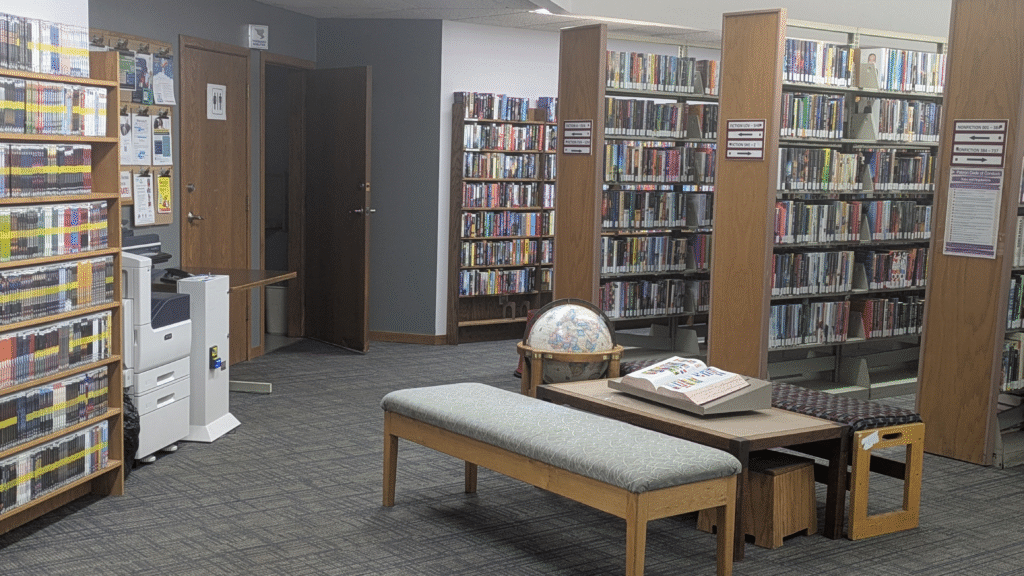 The inside of the library, with shelves, a copy machine, a globe and a bench.