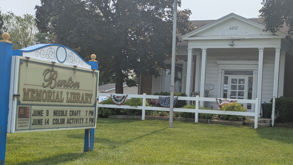 A white building with a sign in front that says Burton Memorial Library.