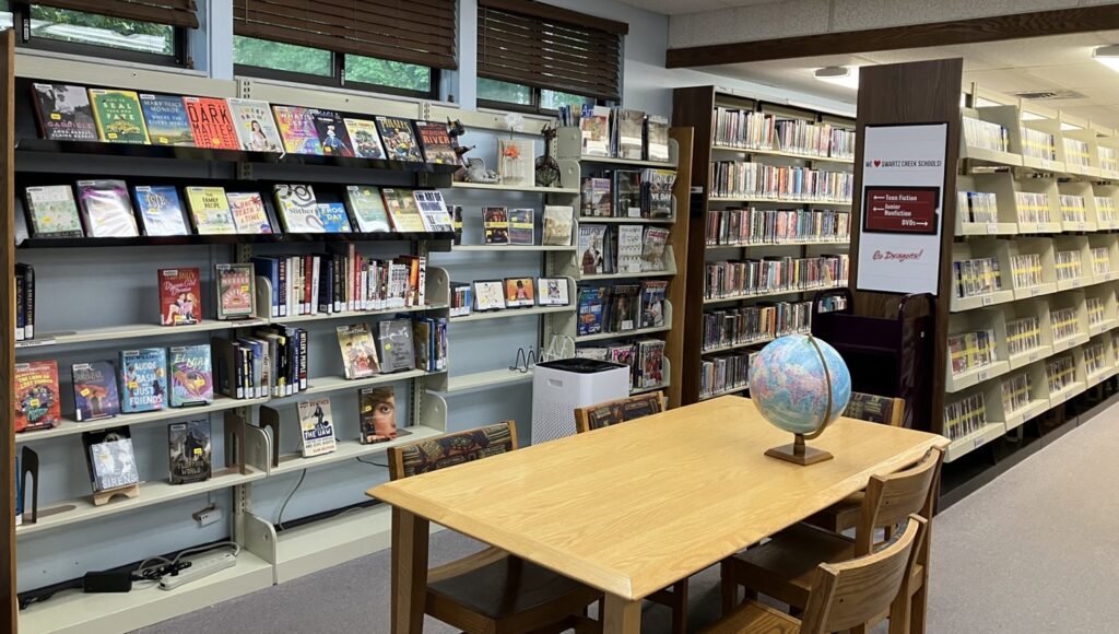 The inside of the library. A table with a globe, and shelves of books and DVDs.